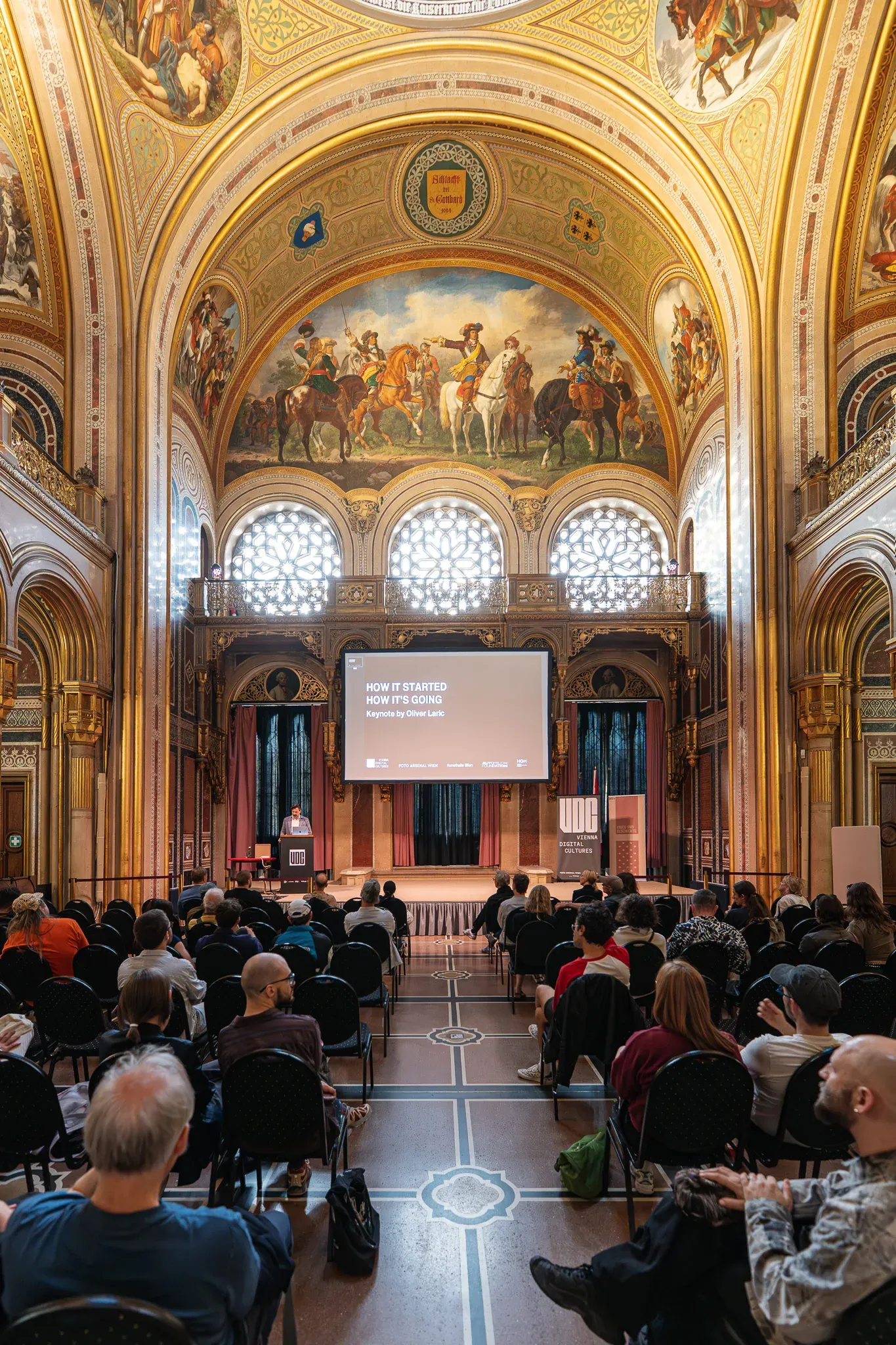 Historischer Festsaal mit Deckenfresko, Publikum von oben.