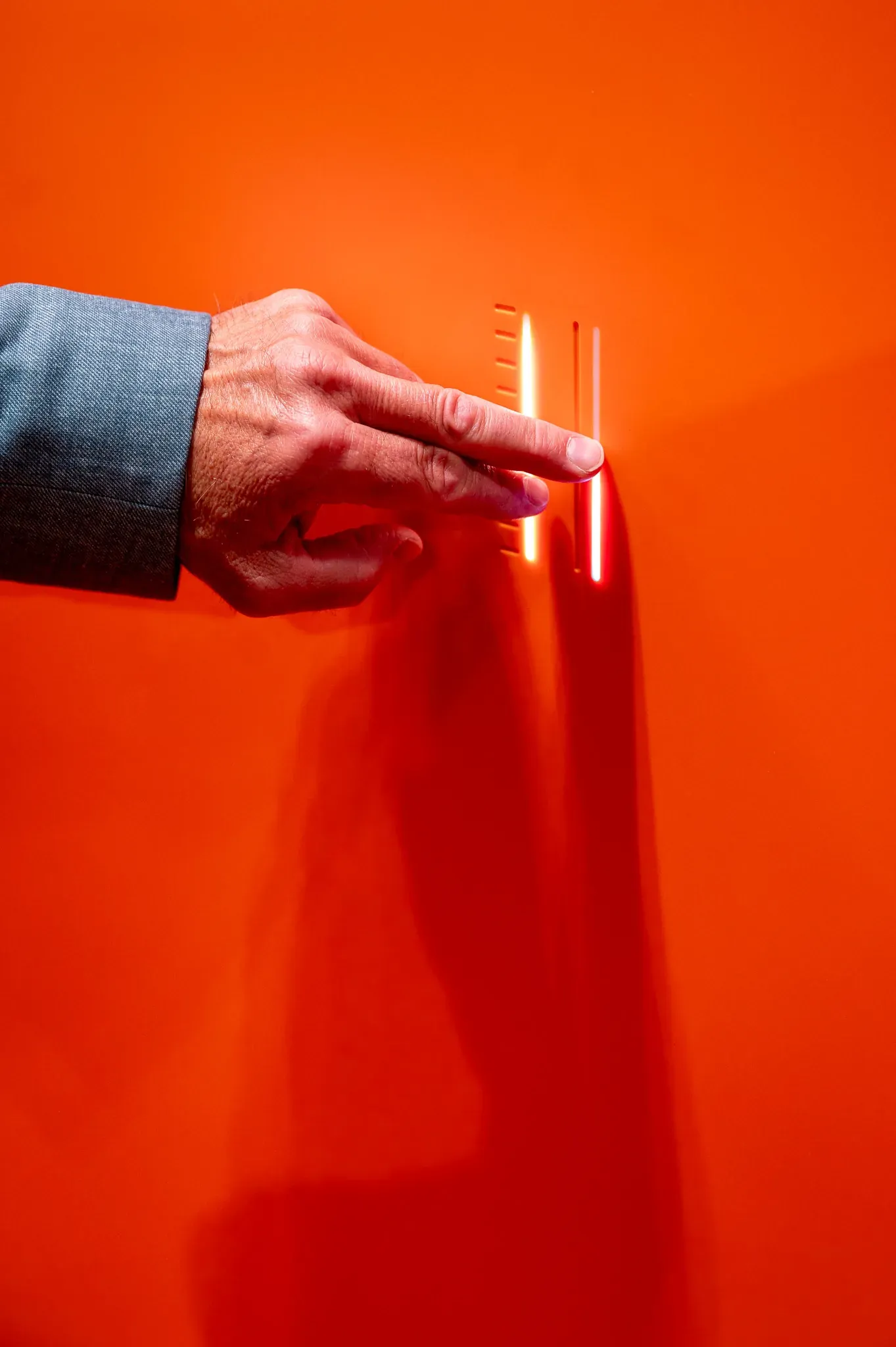 Hand an einer orangefarbenen Wand mit schmalem Objekt.