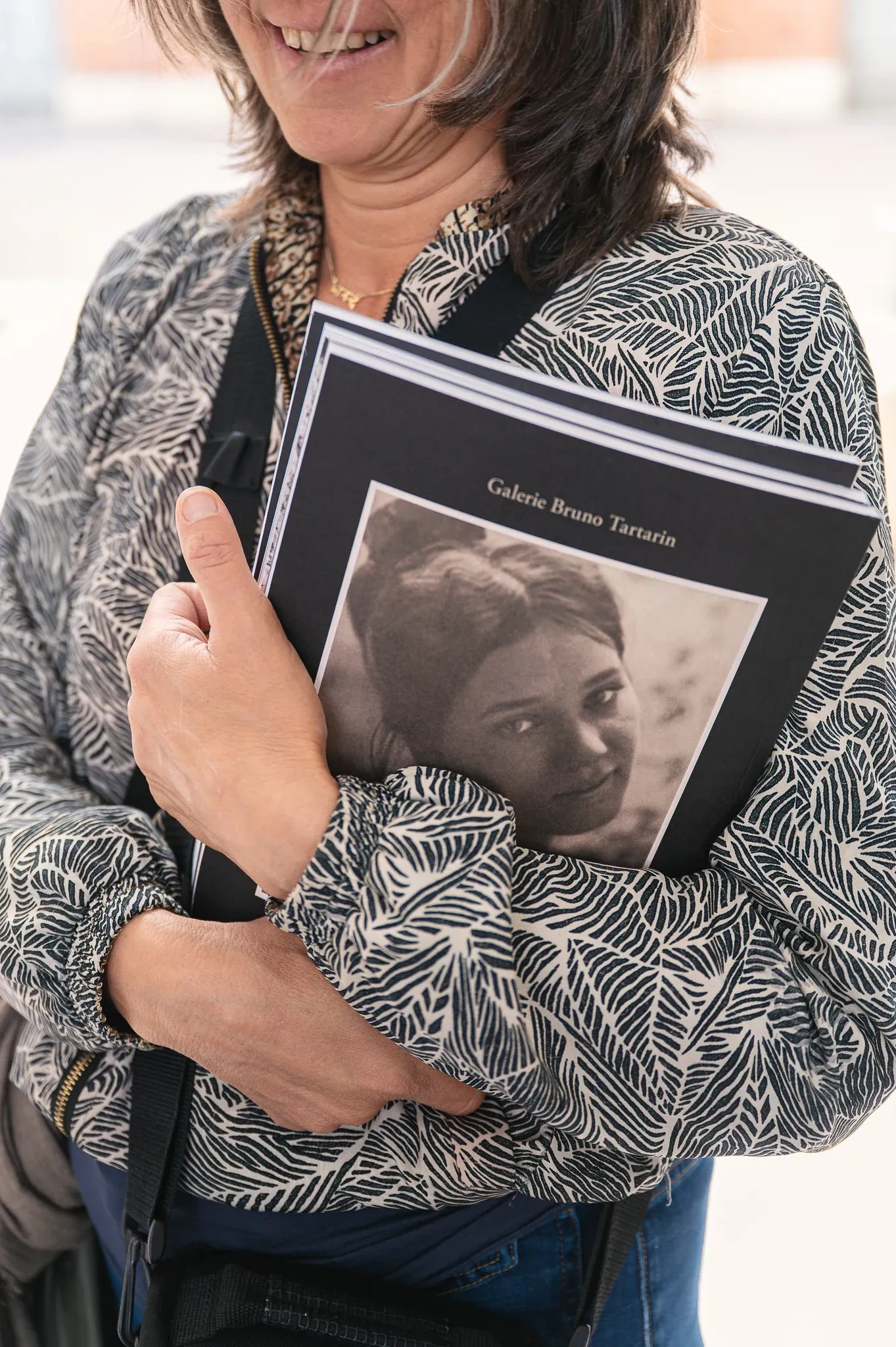 Fotobörse: lachende Besucherin hält ein Fotobuch mit Porträt an sich gedrückt.