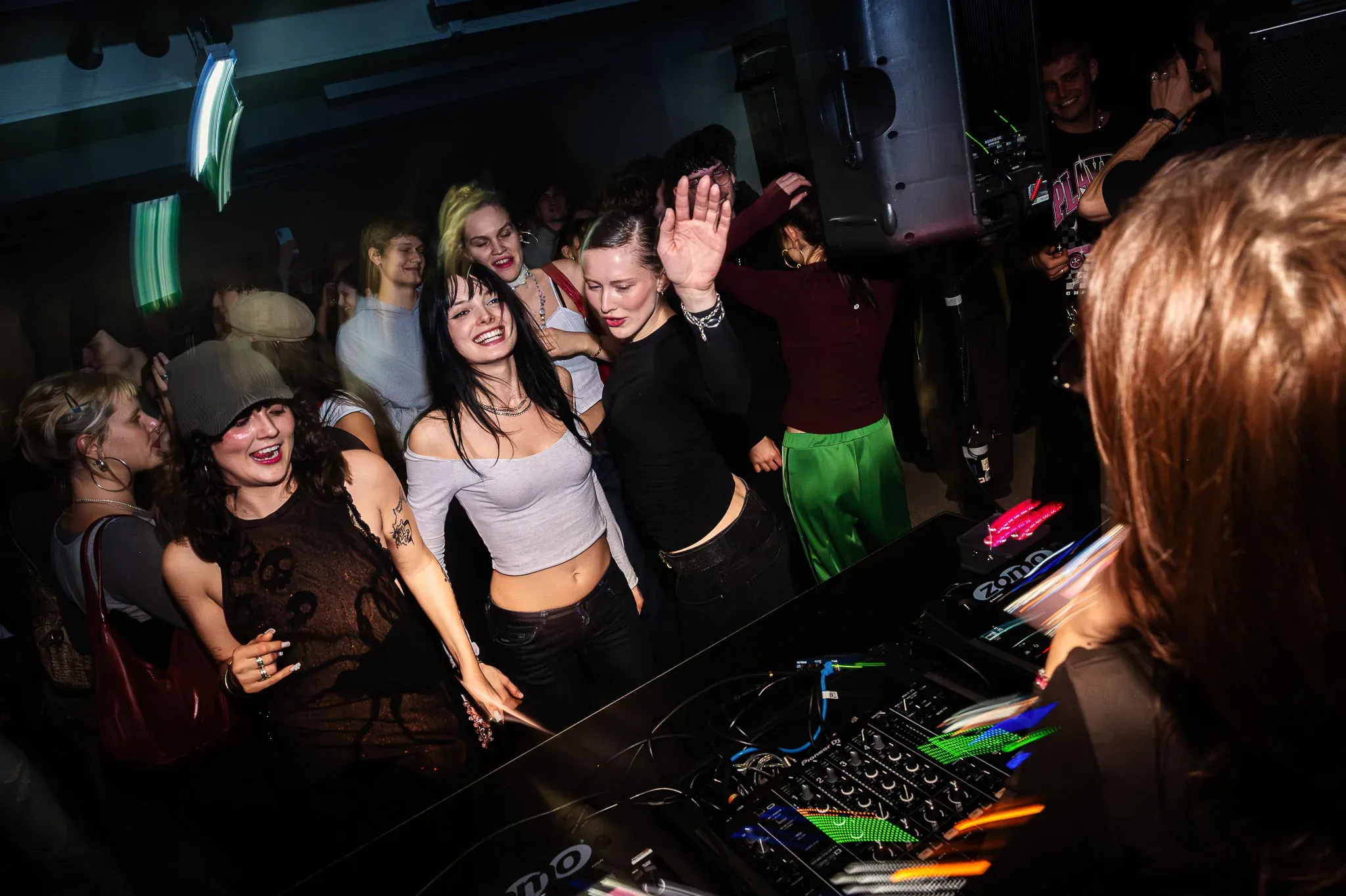 Feiernde Menschen vor dem DJ-Pult in blauem Clublicht.