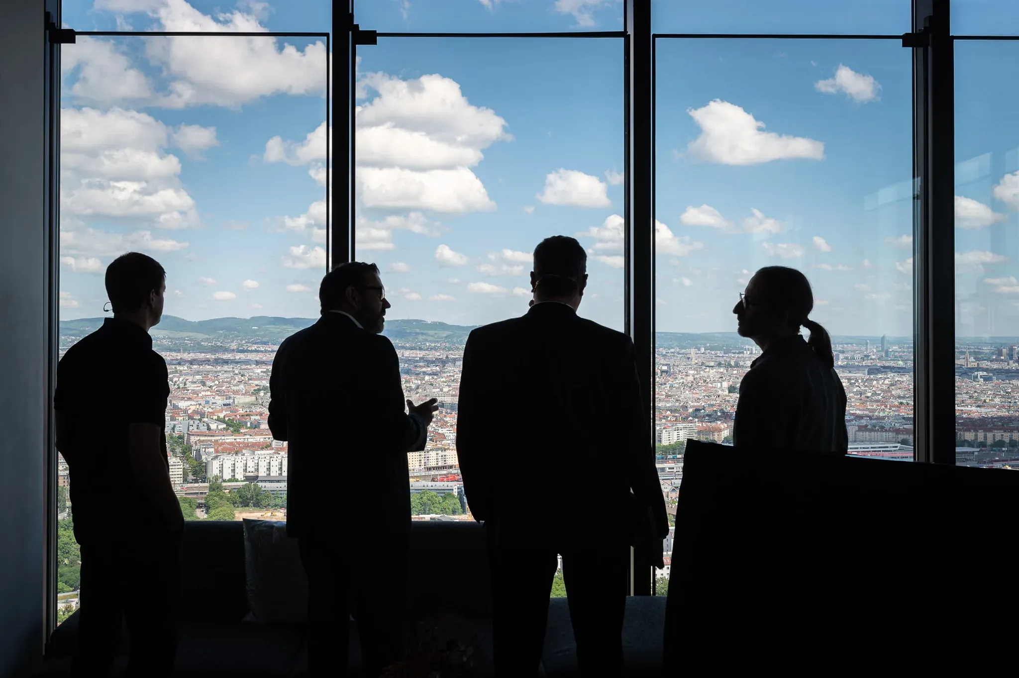 Vier Personen als Silhouetten vor einer Panoramafensterfront über Wien.