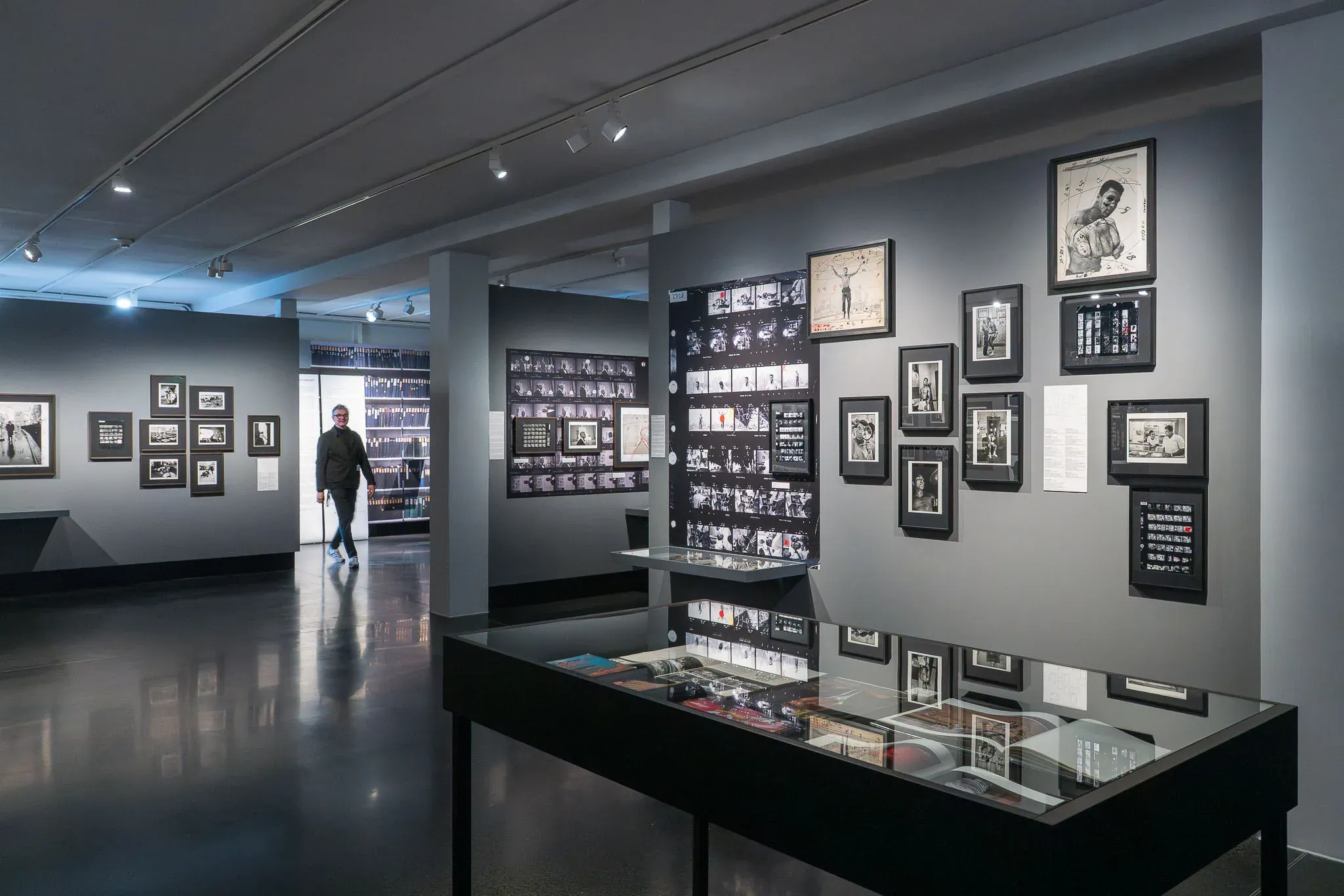 Ausstellungsraum mit Vitrinen und dicht gehängten Fotografien.