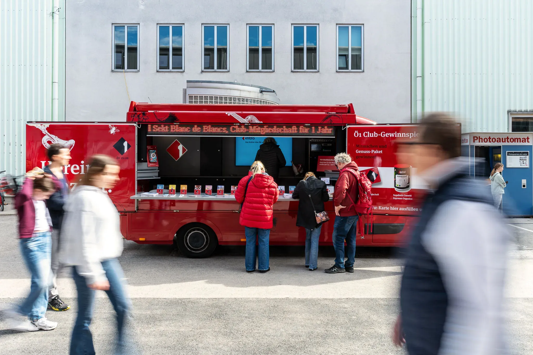Roter Foodtruck vor einem Veranstaltungsgelände, Gäste in Bewegung.
