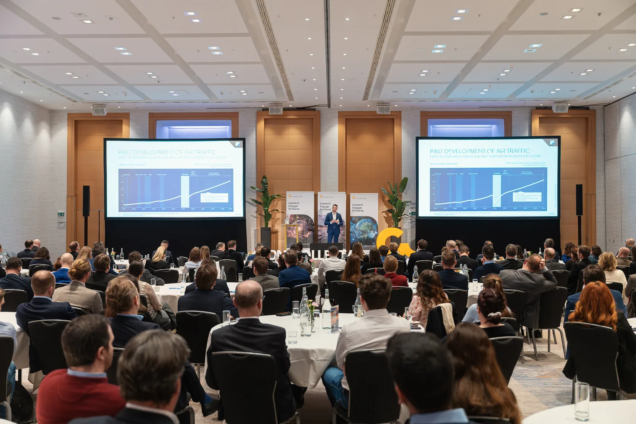Konferenz mit runden Tischen und zwei Präsentationsleinwänden.